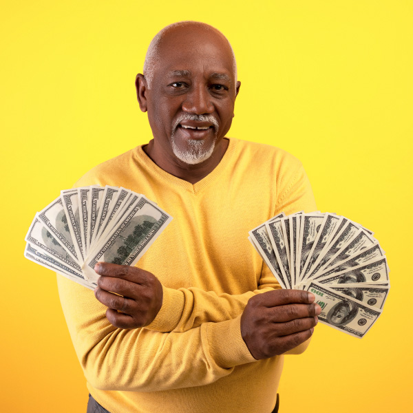older african american male in bright yellow shirt holding fans of cash in each hand and smiling